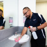 Namoli cleaning professional performing touch point cleaning on a high-contact bathroom surface using TGA-approved disinfectant.